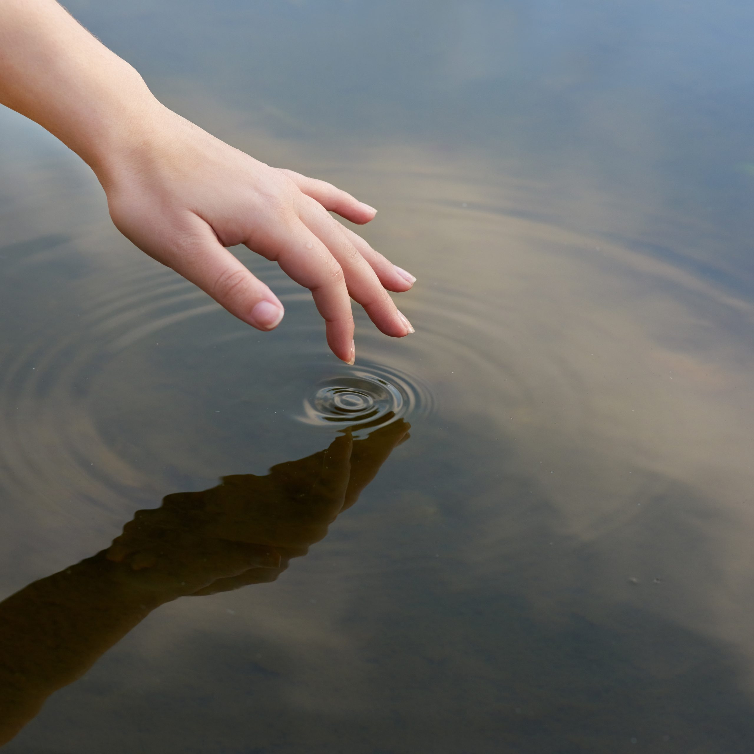 Patterns in a pond. Cropped shot of a finger touching water to form ripples